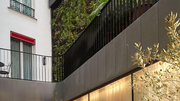 A modern outdoor seating area with multiple tables and chairs, surrounded by potted plants and a glass wall. - Villa-des-Prés (Paris)