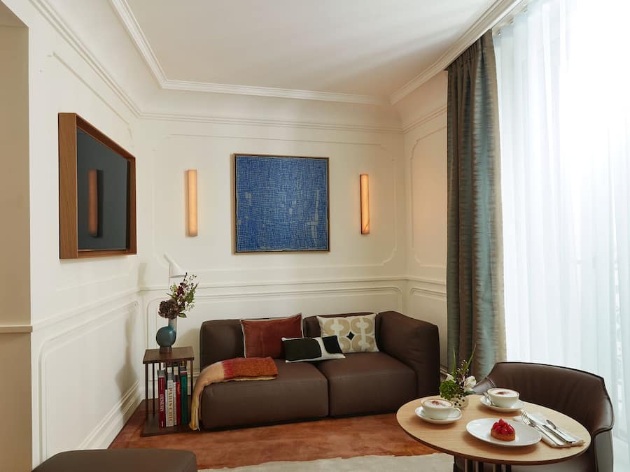 A modern living room with a brown sofa, a coffee table, and a dining area with a chair and plates of food.
