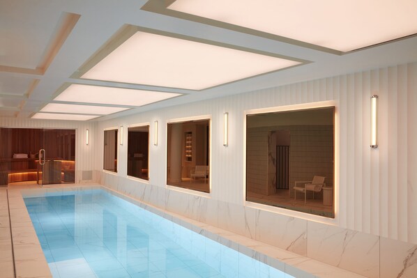 A modern indoor swimming pool with clear glass walls, recessed lighting, and a clean, minimalist design. - Villa-des-Prés (Paris)