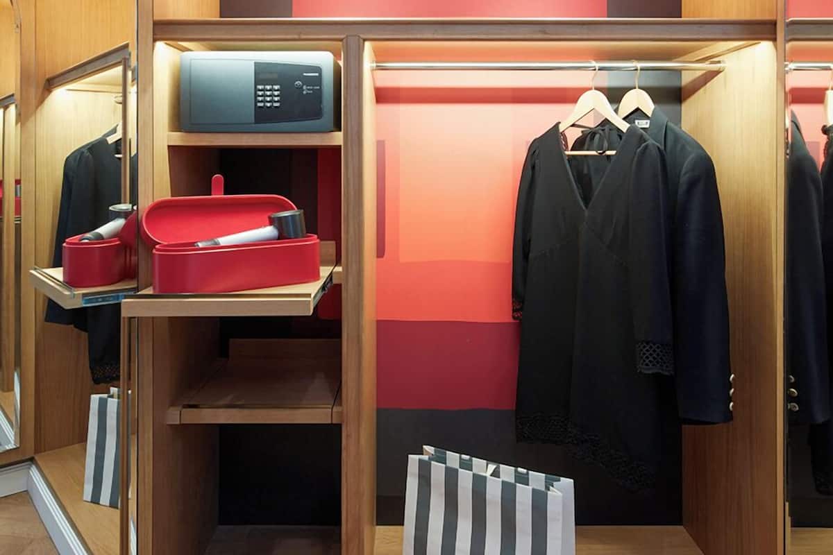 Un armario pequeño y ordenado con puertas de espejo, un microondas y ropa y accesorios bien organizados.