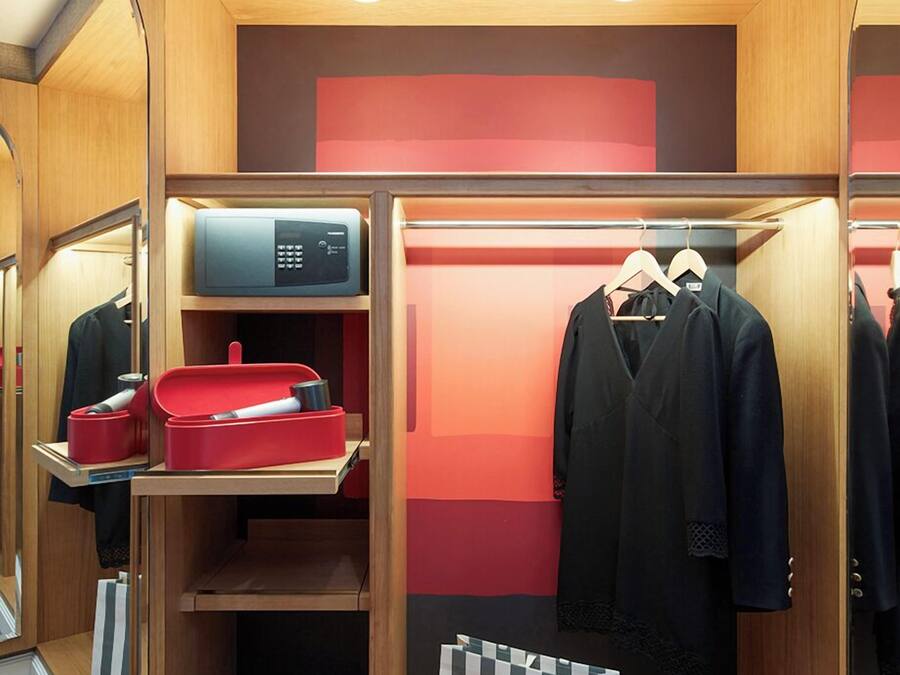 A compact, well-organized closet with mirrored doors, a microwave, and neatly arranged clothing and accessories.
