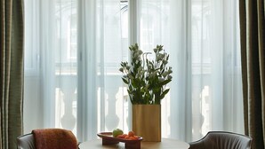 A dining area with a round table, two chairs, a vase with flowers, and a pendant light. - Villa-des-Prés (Paris)