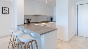 A modern kitchen with a central island, bar stools, and white cabinetry. - Apartment 'Ground Floor 2bed Miradores Del Sol' with Shared Pool, Wi-Fi and Air Conditioning (Estepona)