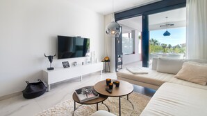 A modern living room with a flat-screen TV, a sofa, a coffee table, and a view of the outdoors. - Apartment 'Ground Floor 2bed Miradores Del Sol' with Shared Pool, Wi-Fi and Air Conditioning (Estepona)
