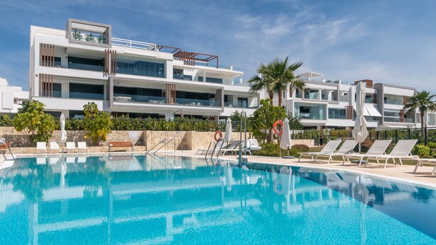 A modern hotel with a pool, sun loungers, and palm trees. - Apartment 'Ground Floor 2bed Miradores Del Sol' with Shared Pool, Wi-Fi and Air Conditioning (Estepona)