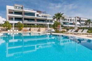 Ein modernes Hotel mit Pool, Liegestühlen und Palmen.