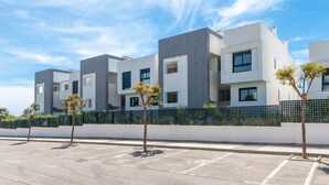 A modern multi-story residential building with a flat roof, large windows, and a parking lot in front. - Apartment 'Ground Floor 2bed Miradores Del Sol' with Shared Pool, Wi-Fi and Air Conditioning (Estepona)