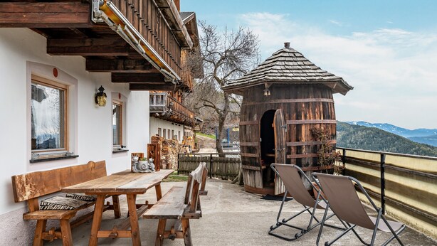 Un bâtiment en bois doté d’un balcon, d’une table avec des bancs et offrant une vue sur les montagnes.