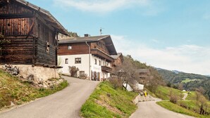 Une route de campagne mène à des maisons traditionnelles en bois dotées de balcons, le tout étant entouré de collines verdoyantes.