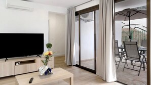 A modern hotel room with a flat-screen TV, a wooden coffee table with a vase, and a sliding glass door leading to a balcony with outdoor furniture. - Vacation Home 'Suite Deluxe Puerto Rico 11' with Shared Pool and Wi-Fi (Puerto Rico)