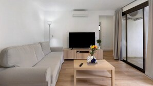 A modern living room with a sofa, a flat-screen TV, a coffee table with a vase, and a sliding glass door. - Vacation Home 'Suite Deluxe Puerto Rico 11' with Shared Pool and Wi-Fi (Puerto Rico)