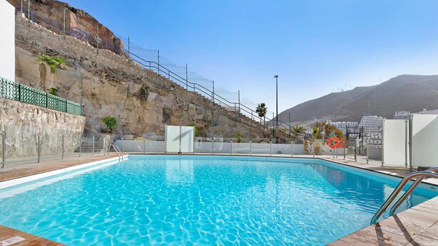 A swimming pool with clear blue water, a stone wall, and a view of a mountain. - Vacation Home 'Suite Deluxe Puerto Rico 11' with Shared Pool and Wi-Fi (Puerto Rico)