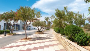 A paved walkway lined with trees and shrubs, leading to a building with a modern design. - Spacious 'Amplio Canet' Apartment with Shared Pool, Wi-Fi, and Air Conditioning (Canet de Berenguer)