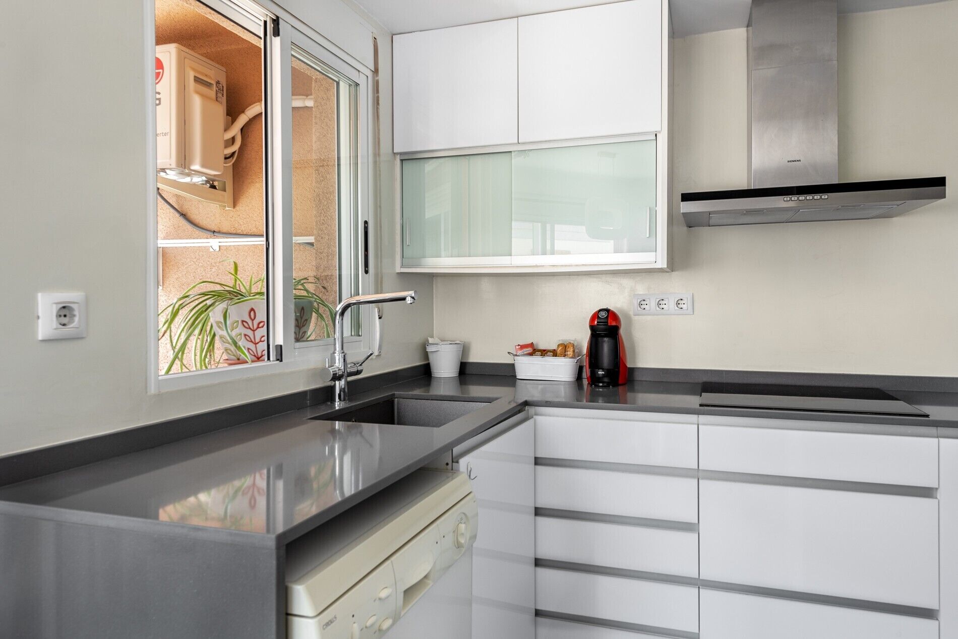 Una cocina moderna con lavavajillas incorporado, cafetera y ventana con vistas al exterior.