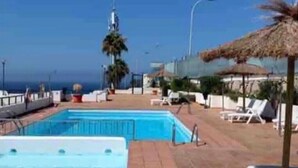 Une piscine avec une terrasse carrelée, des chaises longues et une vue sur l’océan.