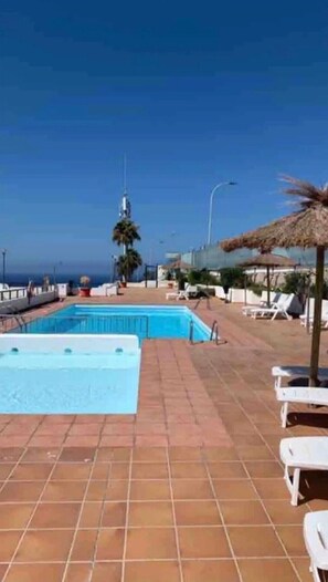 A swimming pool with a tiled deck, lounge chairs, and a view of the ocean.
