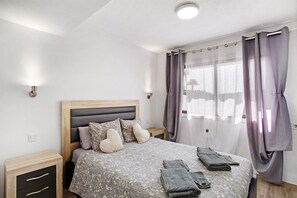 Une chambre à coucher avec un lit, des tables de chevet, une fenêtre avec des rideaux et une tête de lit.