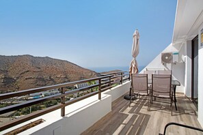 A balcony with a view of a mountainous landscape, a table with chairs, and an umbrella.