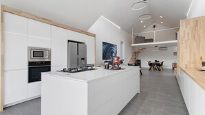 Une cuisine moderne avec des meubles blancs, un îlot central, un four encastré et une machine à café.