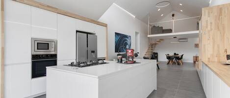 Een moderne keuken met witte kastjes, een centraal eiland, een inbouwoven en een koffieapparaat.
