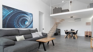 Un salon moderne avec un canapé gris, une table basse en bois, un coin repas avec une table et des chaises en bois, un escalier et un grand tableau abstrait accroché au mur.