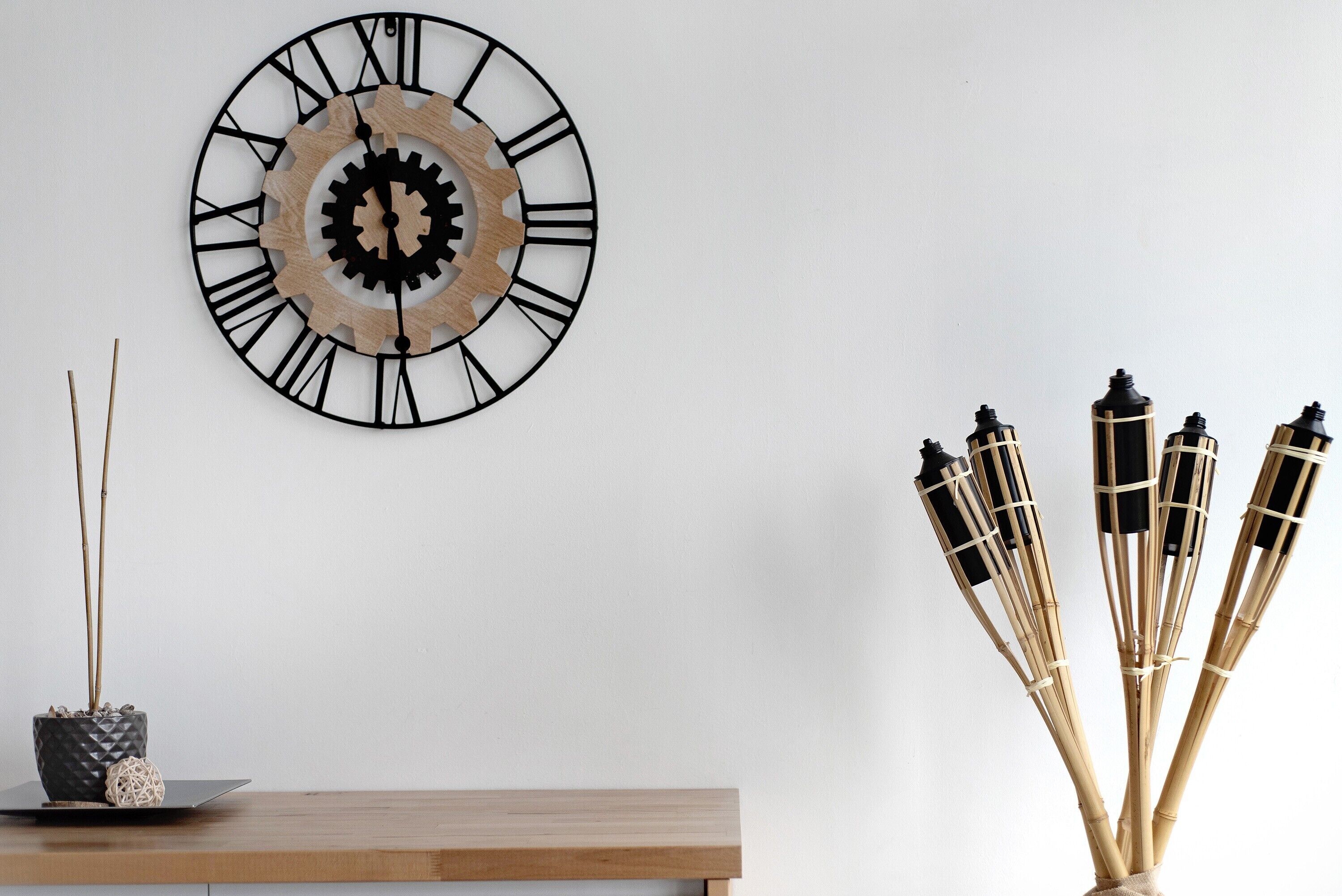 Un reloj de pared con números romanos, una pequeña planta en maceta y un arreglo decorativo de bambú sobre una superficie de madera.