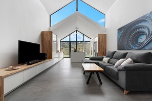Un salon moderne doté d’un téléviseur à écran plat, d’un canapé gris, d’une table basse en bois et d’une grande fenêtre.