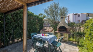 An outdoor patio with a table set for dining, surrounded by greenery and a stone pathway. - Holiday Home 'Villetta Sarda' with Private Terrace and Air Conditioning (san teodoro lu fraili)