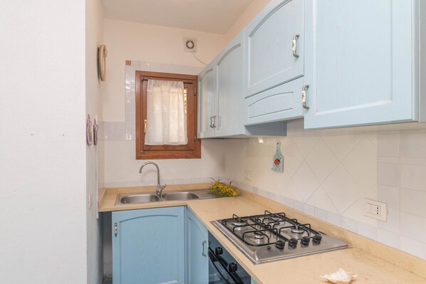 A kitchen with blue cabinets, a gas stove, a sink, and a window with a curtain.