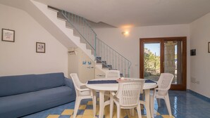 A room with a blue sofa, a white table with chairs, a staircase with blue railings, and a door leading outside. - Holiday Home 'Villetta Sarda' with Private Terrace and Air Conditioning (san teodoro lu fraili)