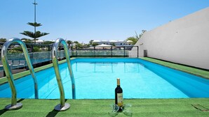 Una piscina amb aigua turquesa cristal·lina, una ampolla de vi i dues copes al costat de la piscina.