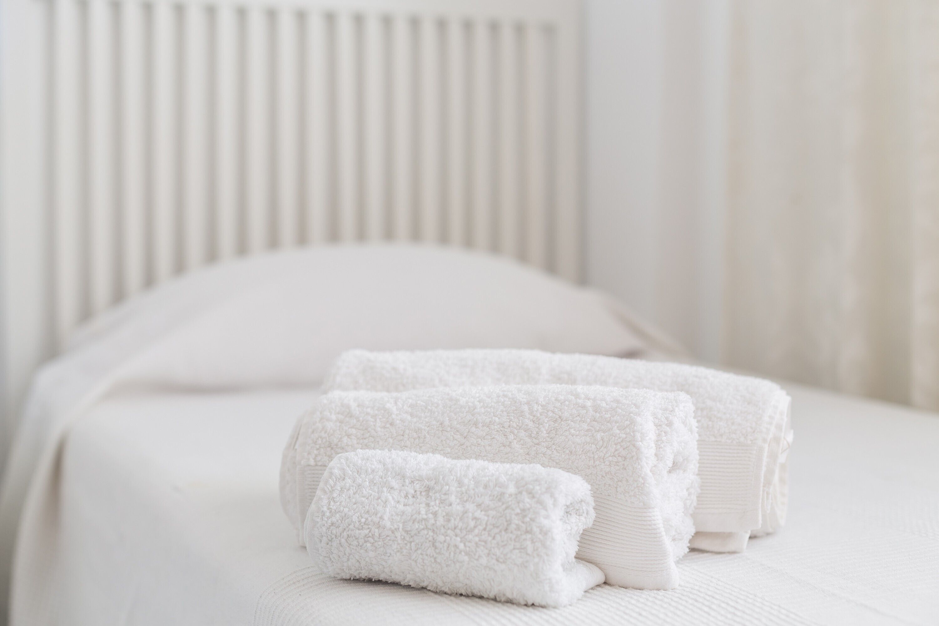 Una cama bien hecha con sábanas blancas y toallas enrolladas.