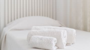 Una cama bien hecha con sábanas blancas y toallas enrolladas.