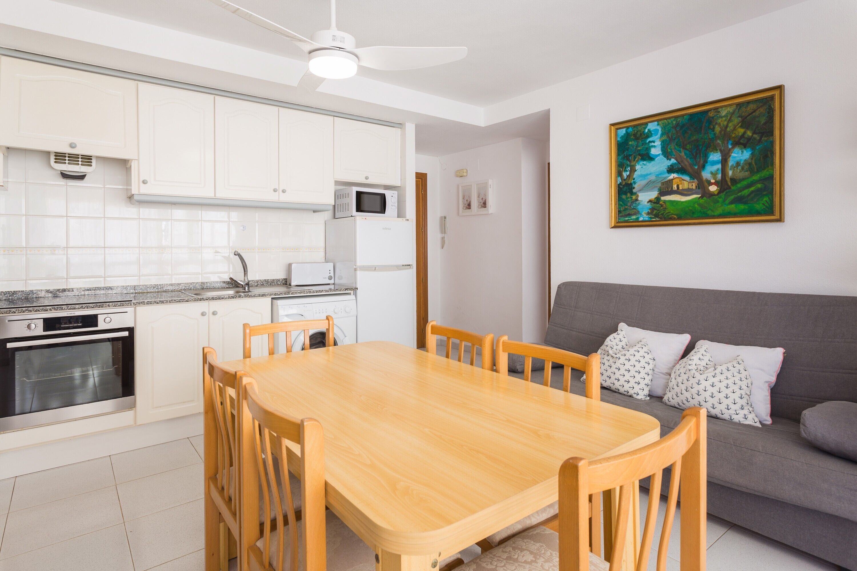 Una cocina moderna con armarios blancos, una mesa de comedor y un sofá gris.