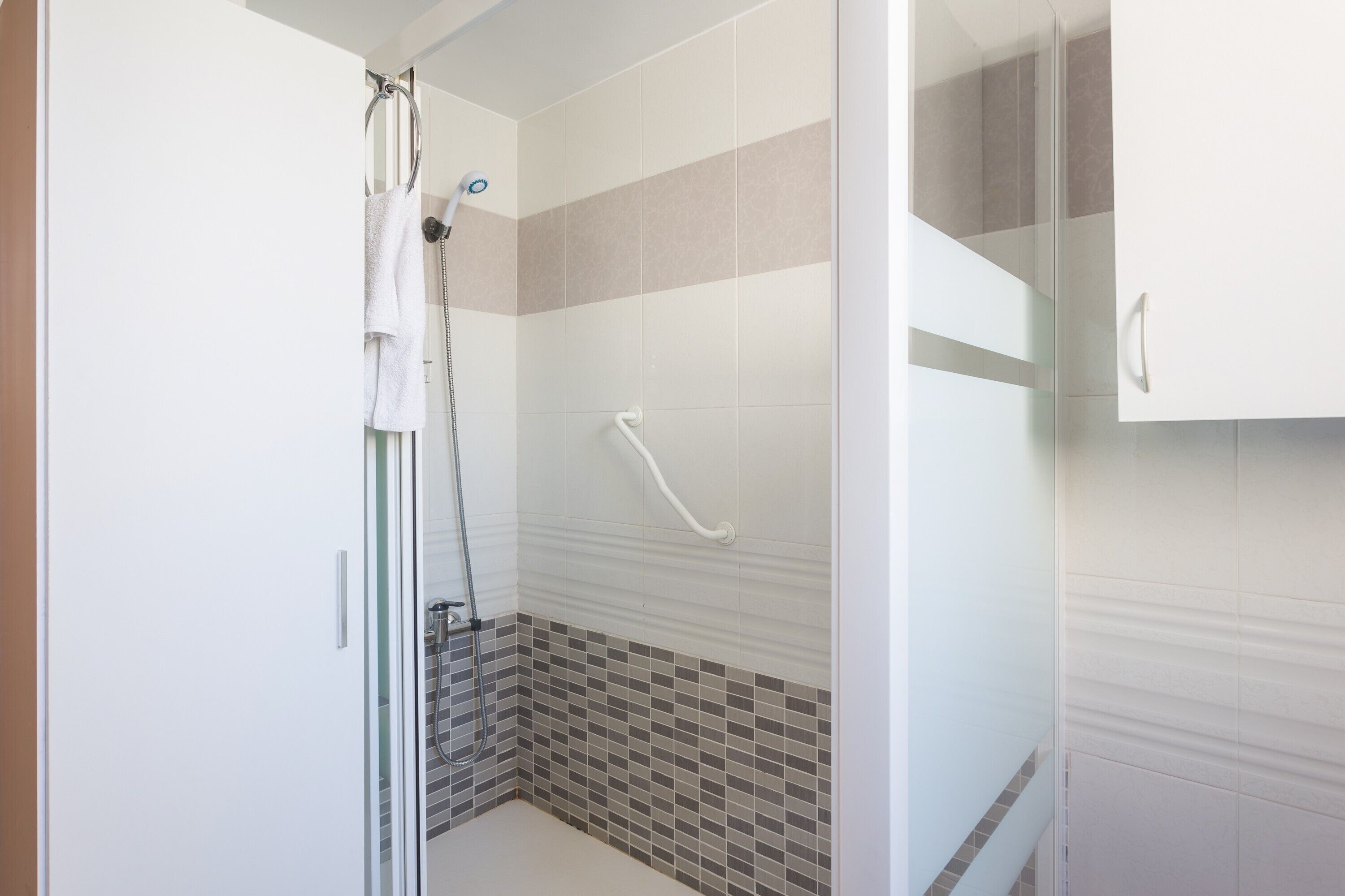 A modern bathroom with a glass shower enclosure, a white towel hanging on the door, and a tiled floor.