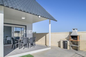 Un patio cubierto con una mesa y sillas, una parrilla de barbacoa y una puerta de cristal que da a un espacio interior.