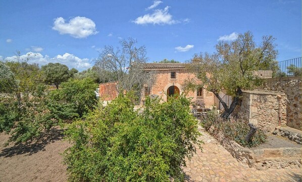 A rustic stone building with a tiled roof, surrounded by greenery and a stone pathway.