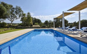 Une piscine rectangulaire à l’eau d’un bleu cristallin, entourée d’un mur de pierre et d’une zone herbeuse.