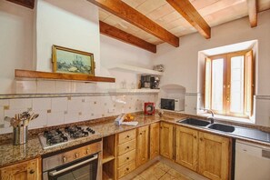 A kitchen with wooden cabinets, a gas stove, a microwave, and a window with blinds.
