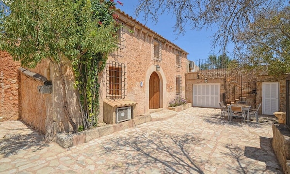 A rustic stone building with a wooden door, a covered outdoor seating area, and a staircase.