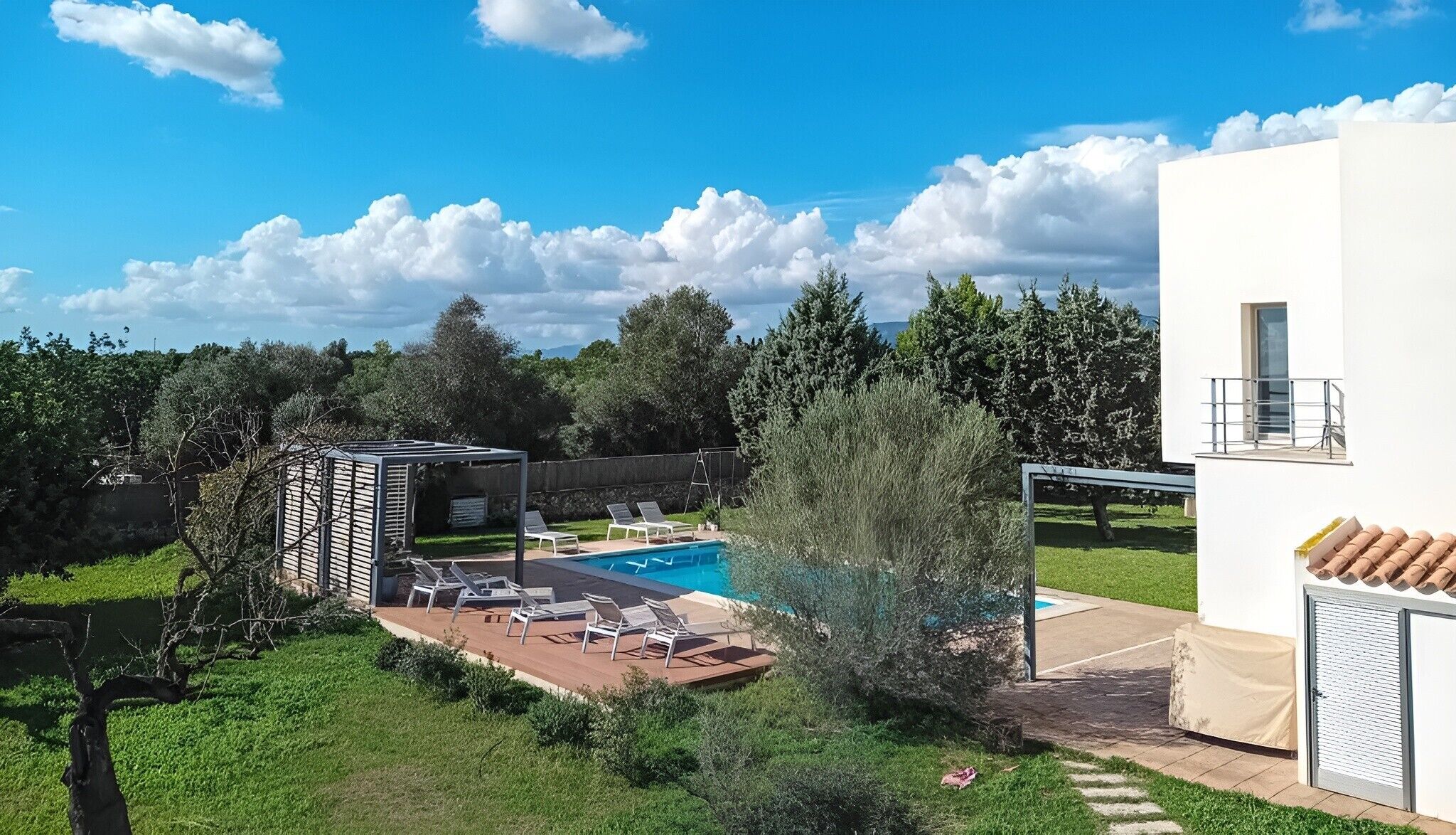 Un espace piscine avec des chaises longues, un petit abri et un bâtiment blanc doté d’un balcon.
