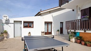 Un cortile con tavolo da ping pong, piante in vaso e un edificio bianco con finestre e un balcone.