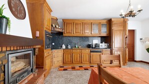 Una cucina con mobili in legno, un camino in mattoni, un tavolo da pranzo con una tovaglia e un orologio appeso al muro.