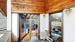 A wooden ceiling, a glass door leading to a room with a table and chairs, and a view of a green landscape. - 4-room apartment in the loft. (Sils/Segl Maria)
