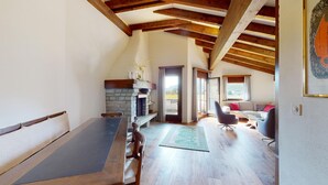 A spacious room with a wooden dining table, a stone fireplace, and a view of the outdoors. - 4-room apartment in the loft. (Sils/Segl Maria)