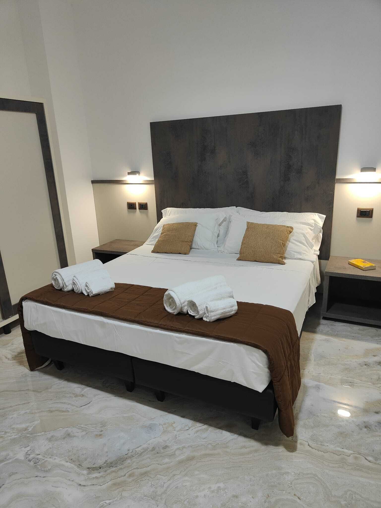 A hotel room with a large bed, two bedside tables, and a marble floor.