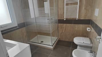 Un bagno moderno con doccia vetro, due servizi igienici, un bidet e un lavandino bianco.