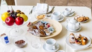 A breakfast setup with a variety of fruits, pastries, and beverages on a table, with a view of a spa area in the background. - HOTEL EBOLI (Eboli)