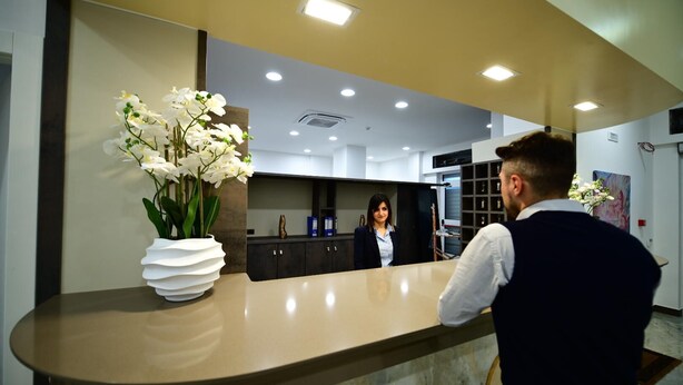 A reception area with a marble counter, a vase of white orchids, and a woman standing behind the counter. - HOTEL EBOLI (Eboli)