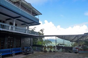 A two-story building with a balcony, a covered outdoor area with potted plants, and a view of the landscape. - Cherry Guest House (Gangtok)